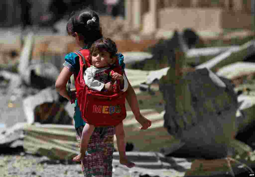 An Iraqi girl carries a baby in a backpack turned into a baby carrier as displaced Iraqis from western Mosul's al-Islah al-Zaraye neighborhood flee their area, during a government forces' military offensive to retake the area from Islamic State (IS) group fighters.