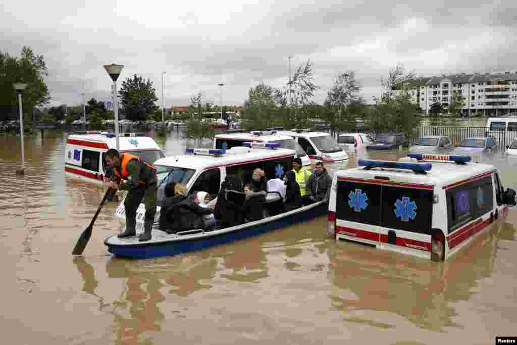 Seorang pria mendayung perahu melewati mobil ambulans yang terendam banjir di Obrenovac, barat daya Belgrad, Serbia (17/5). (Reuters/Marko Djurica)