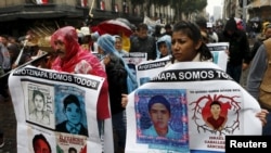 FILE - Relatives and friends hold banners with images of some of the 43 missing students of the Rural Normal School of Ayotzinapa as they march in Mexico City to mark the first anniversary of the students' disappearance, Sept. 26, 2015.