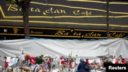 FILE - People mourn in front of the screened-off facade of the Bataclan Cafe adjoining the concert hall, one of the sites of the deadly attacks in Paris, France, a day before a ceremony to pay tribute to the 130 victims, Nov. 26, 2015.