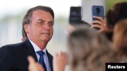 FILE - Brazil's President Jair Bolsonaro poses for pictures as he leaves the Alvorada Palace in Brasilia, Brazil Dec. 12, 2019.