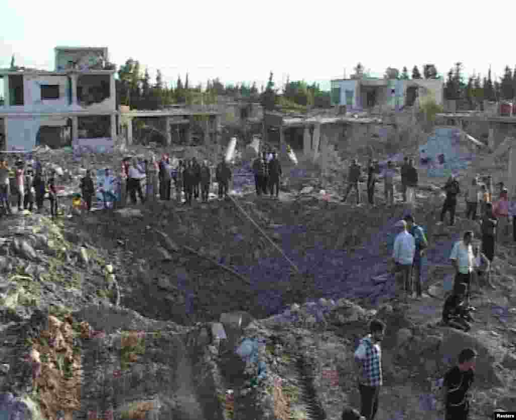 People gather around a crater in Hama city, Syria June 20, 2014, in this picture released by Syria's national news agency SANA.