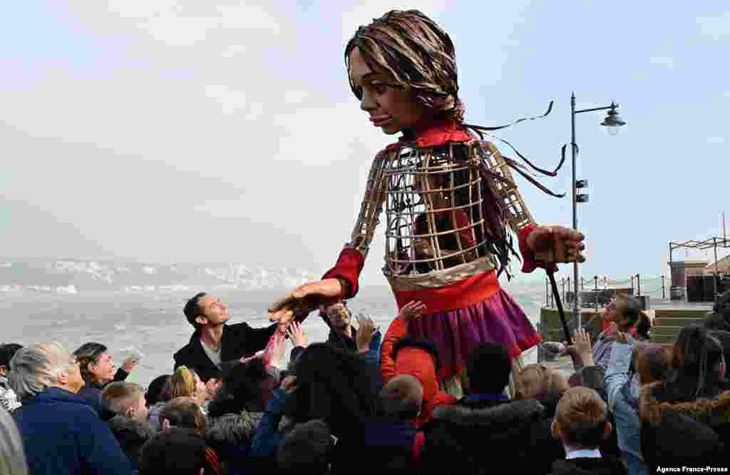 English actor Jude Law holds the hand of 'Little Amal', a giant puppet depicting a Syrian refugee girl, as she walks along the sea front at the harbor in Folkestone, south east England, after arriving from Calais, as part of the international art project The Walk.