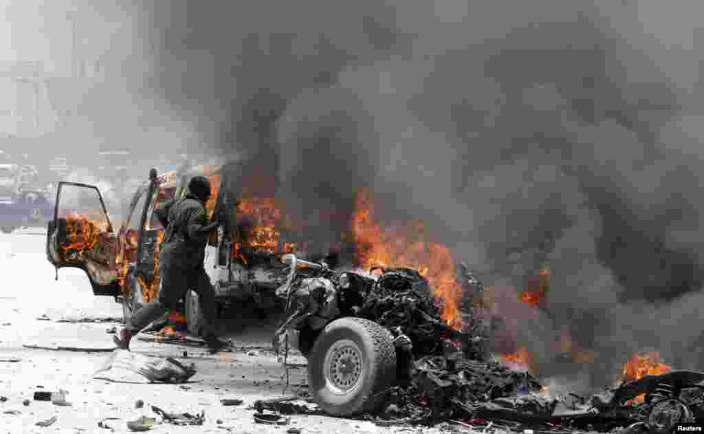 A policeman runs through burning vehicles at the scene of an explosion in Mogadishu, Somalia, March 18, 2013.