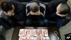 FILE - Suspects, hiding their faces, are held during a gambling raid in China.