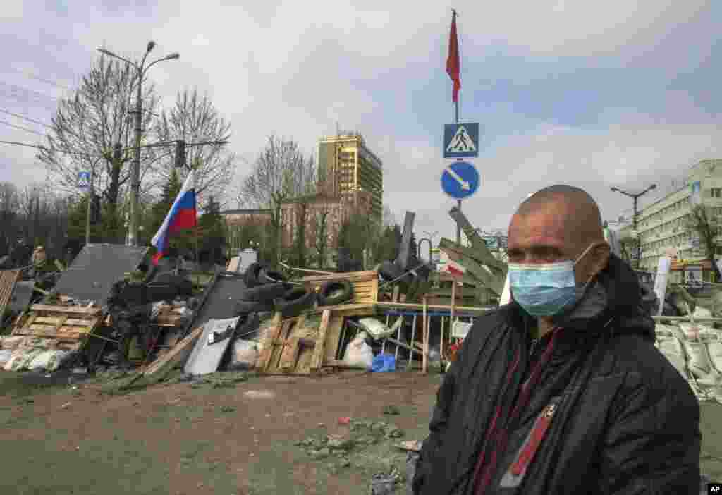 A masked man stands in front of barricades and Soviet era red and Russian national flags at an entrance to the regional office of the security service in Luhansk, Ukraine, April 9, 2014.